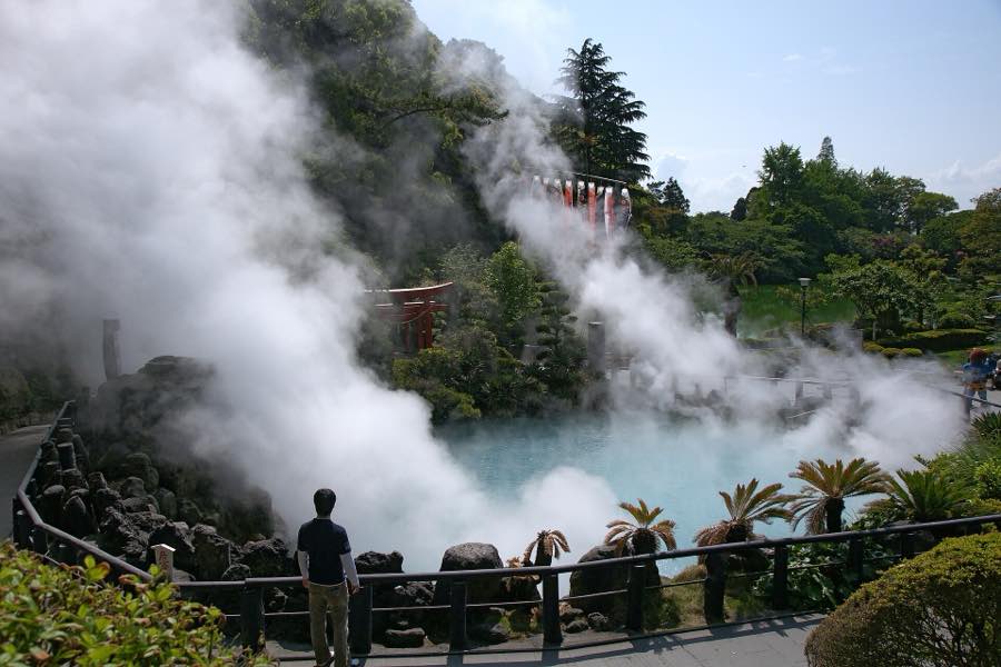 Steam rising from the turquoise pool of Umi Jigoku in Beppu, with a red torii behind